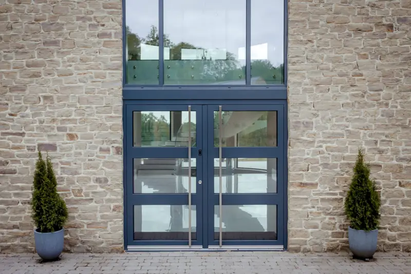 Spitfire S500 aluminium double entrance doors with glazed overhead panel in a stone elevation