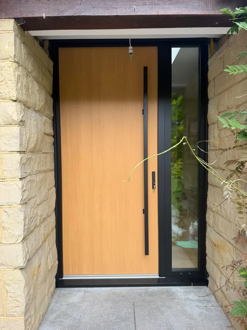 Oak-finish aluminium entrance door with black frame and glazed sidelight installed by Team Frames Trade & Retail